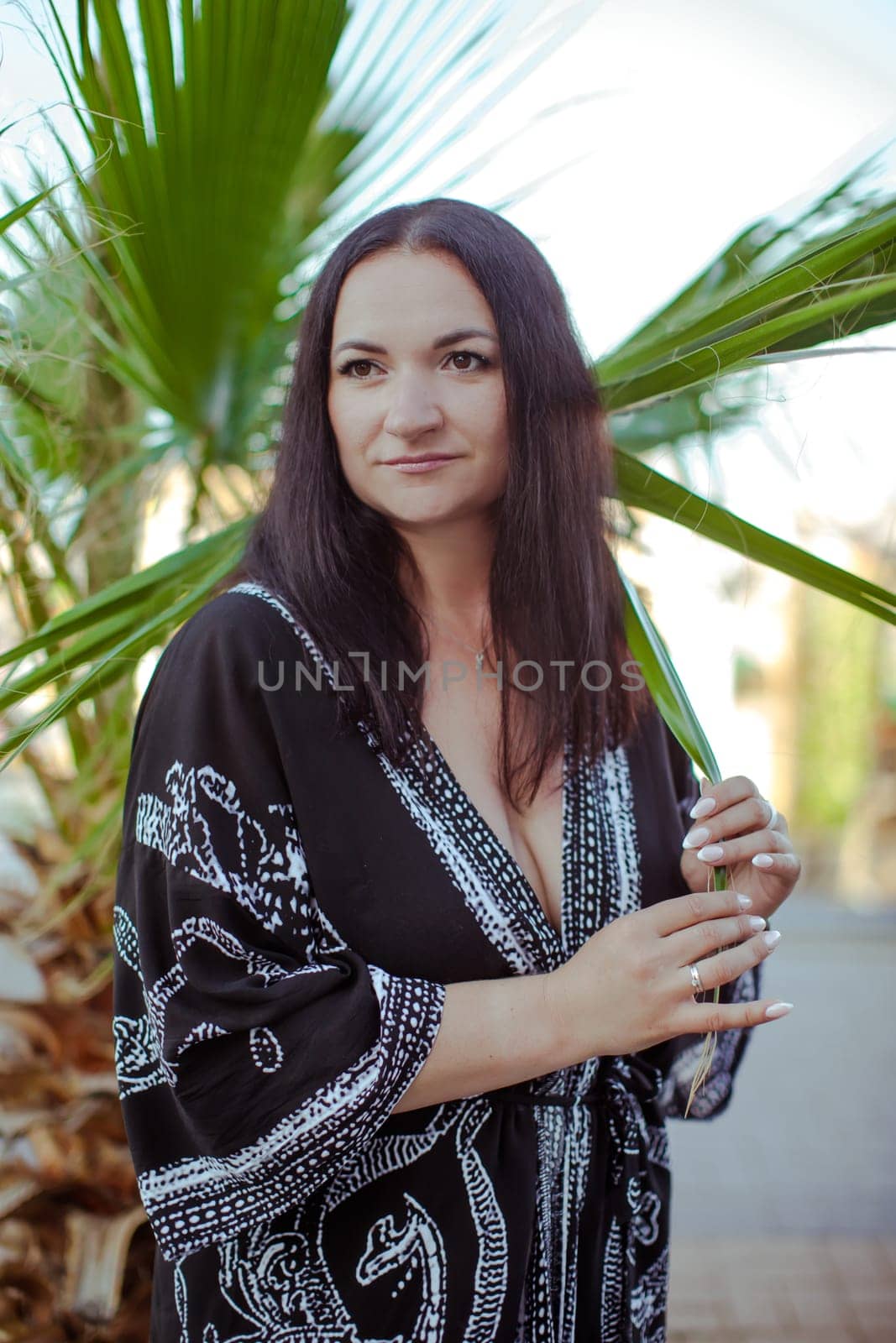 A brunette girl in a black oriental cape stands near a green palm tree