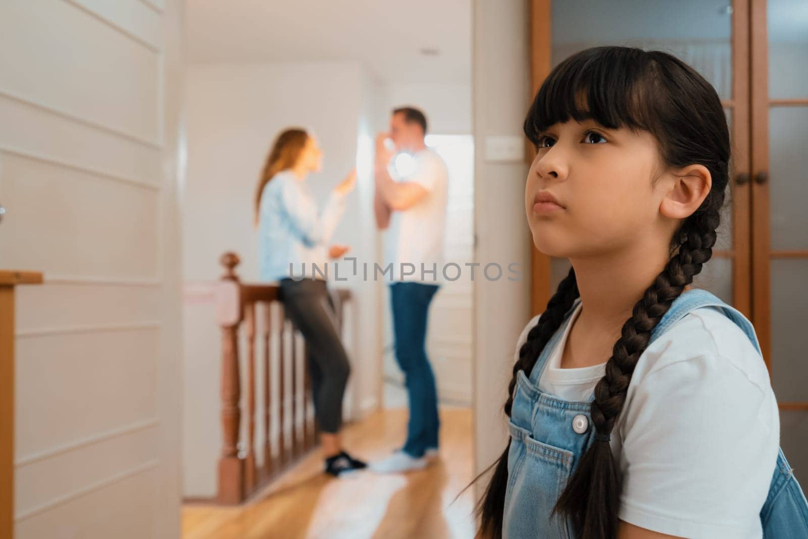 Stressed and unhappy young girl huddle in corner crying and sad while her parent arguing in background. Domestic violence at home and traumatic childhood develop to depression. Synchronos