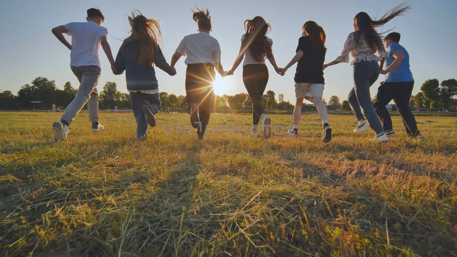 School friends running across the field holding hands at sunset