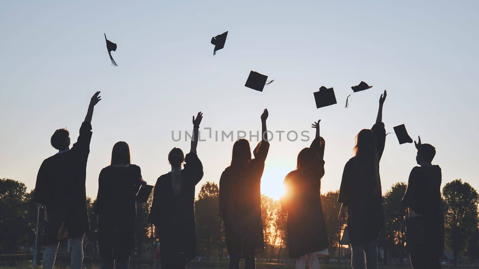 Silhouettes of Happy college graduates tossing their caps up at sunset