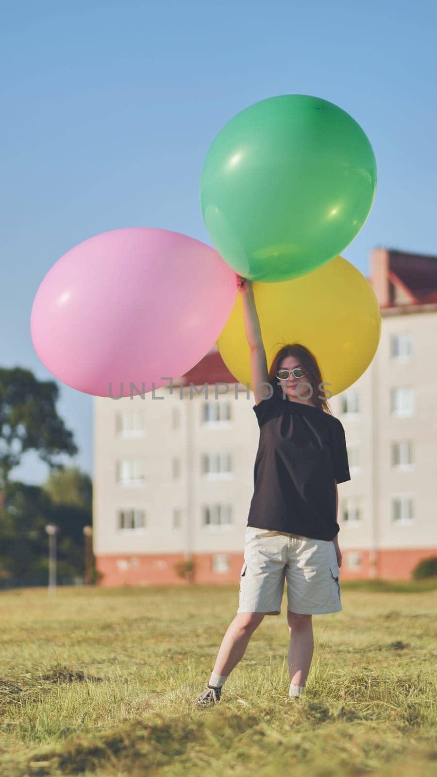 A girl happily poses with large with colorful balloons in the city. Vertical video for smartphone. by DovidPro