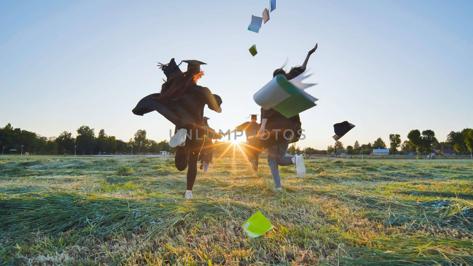 Cheerful graduates students run throwing notebooks after school at sunset