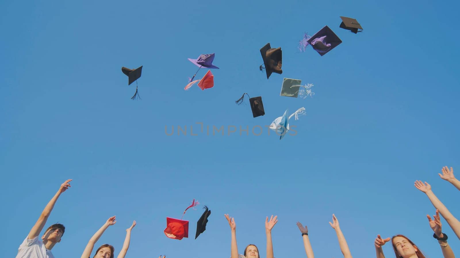 Graduates tossing multicolored hats against a blue sky