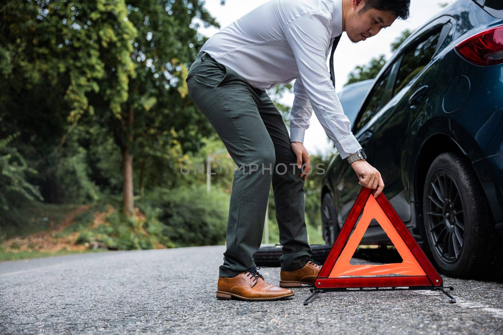 Asian businessman on side of road with broken down red warning triangle. Young male having problem with her car, it stopped on the street. Stranded at Roadside and Waiting for Help.