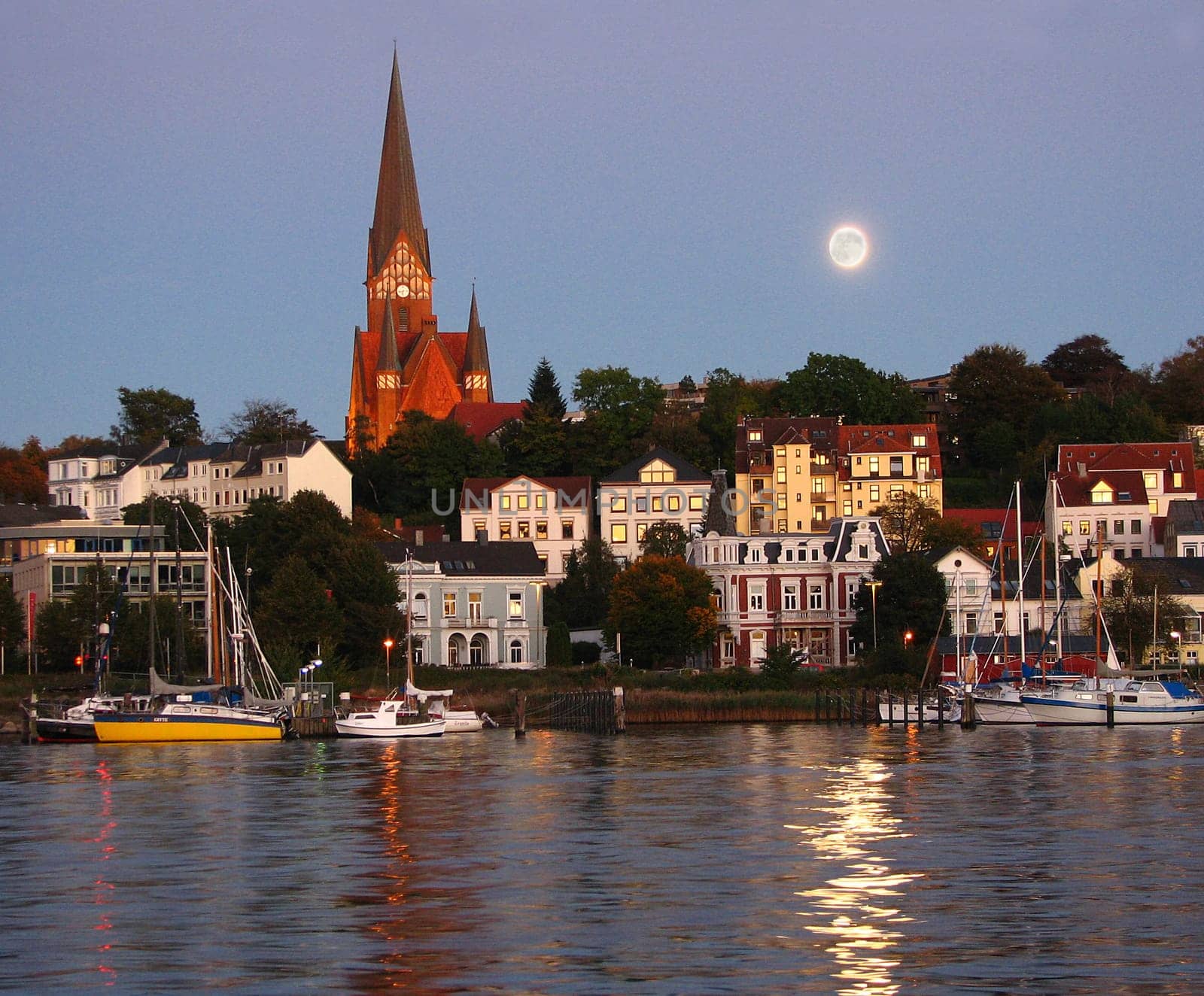 Jürgensby (district of Flensburg) is illuminated by the evening sun and at the same time the moon is reflected in the water.