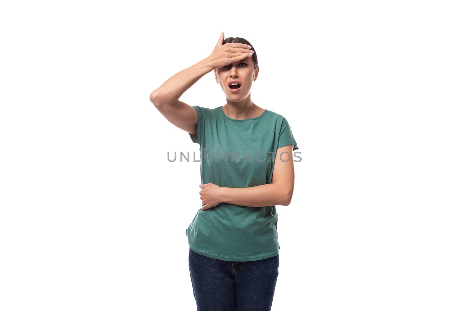 30 year old brunette woman with ponytail dressed in a green basic T-shirt is worried and holding her head.