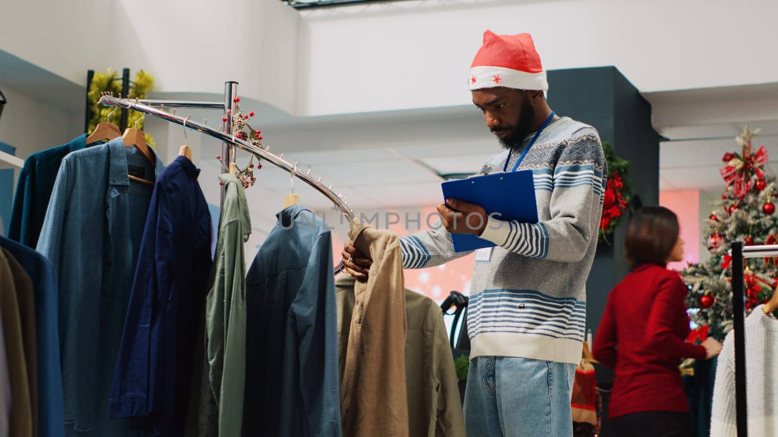 Retail manager browsing through clothing racks in Christmas decorated fashion store, crosschecking price tags with clipboard list. Supervisor inspecting stylish blazers, looking for defects