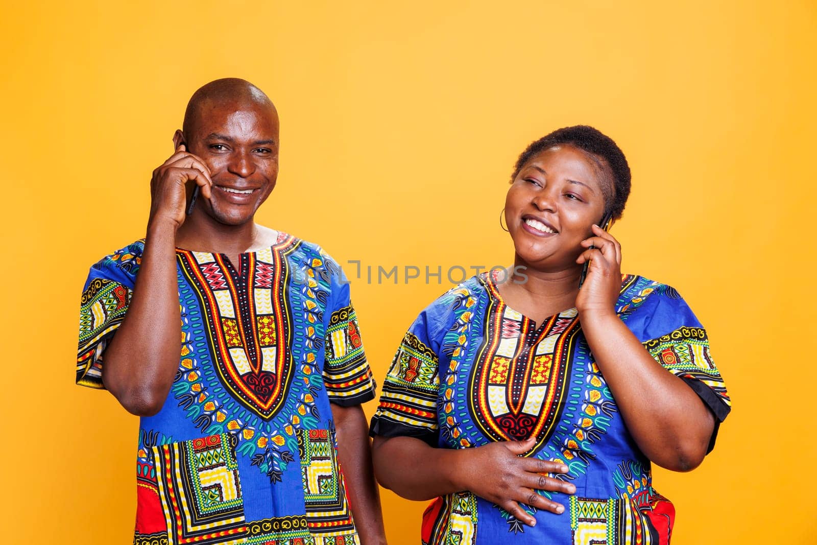 Cheerful african american couple wearing ethnic clothes chatting on smartphone. Smiling mature man and woman answering smartphone call and having fun communication portrait
