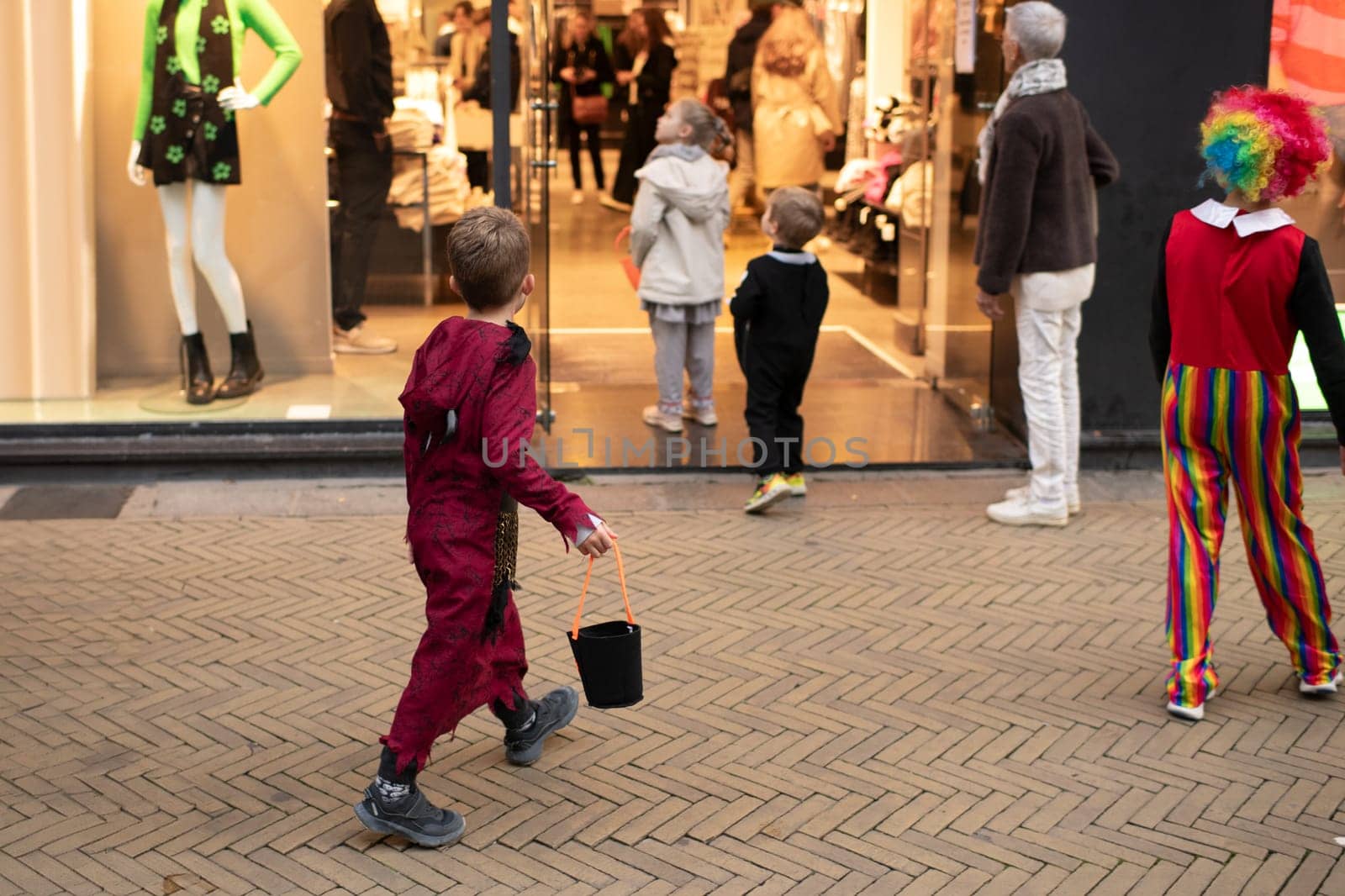 The kids dressed up in the city on Halloween asking for candy in a shop by Godi