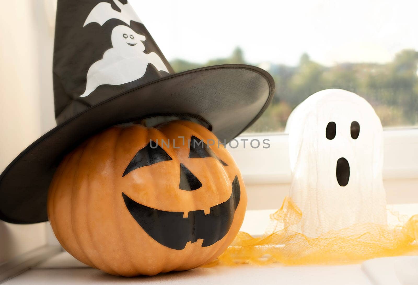 Halloween concept. A pumpkin with a face painted with a black marker and a white ghost against the background of a window in a home interior. Close-up