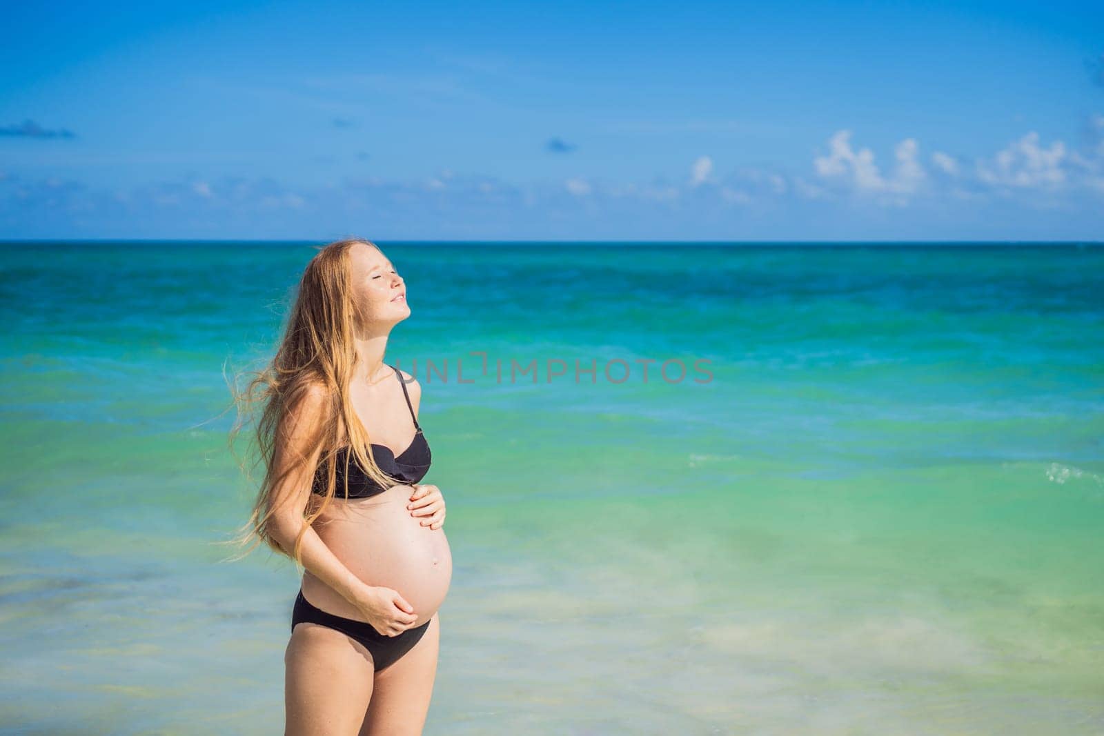 Radiant pregnant woman in a swimsuit, amid the stunning backdrop of a turquoise sea. Serene beauty of maternity by the shore by galitskaya