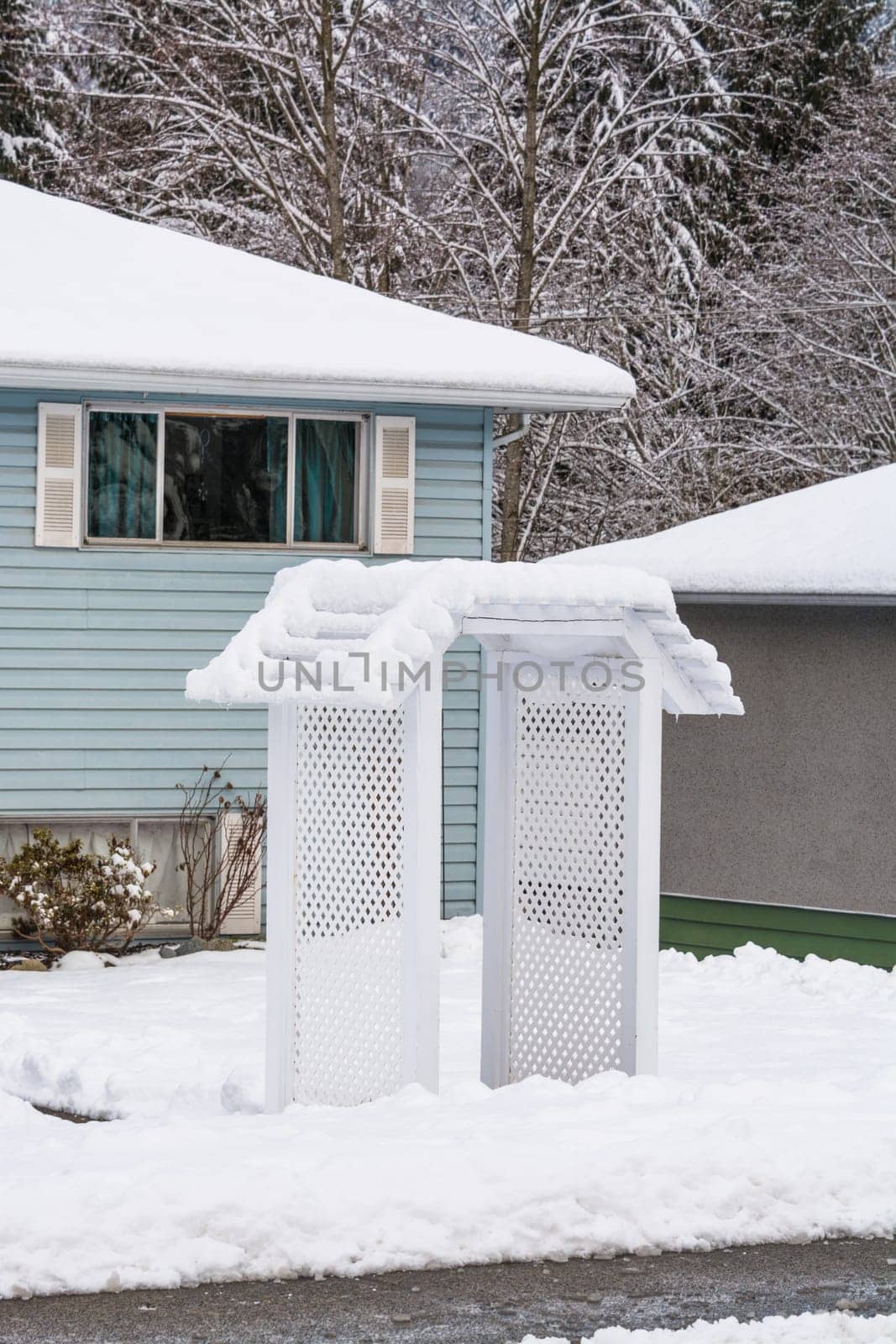 Residential house front yard in snow with entrance arch over pathway by Imagenet