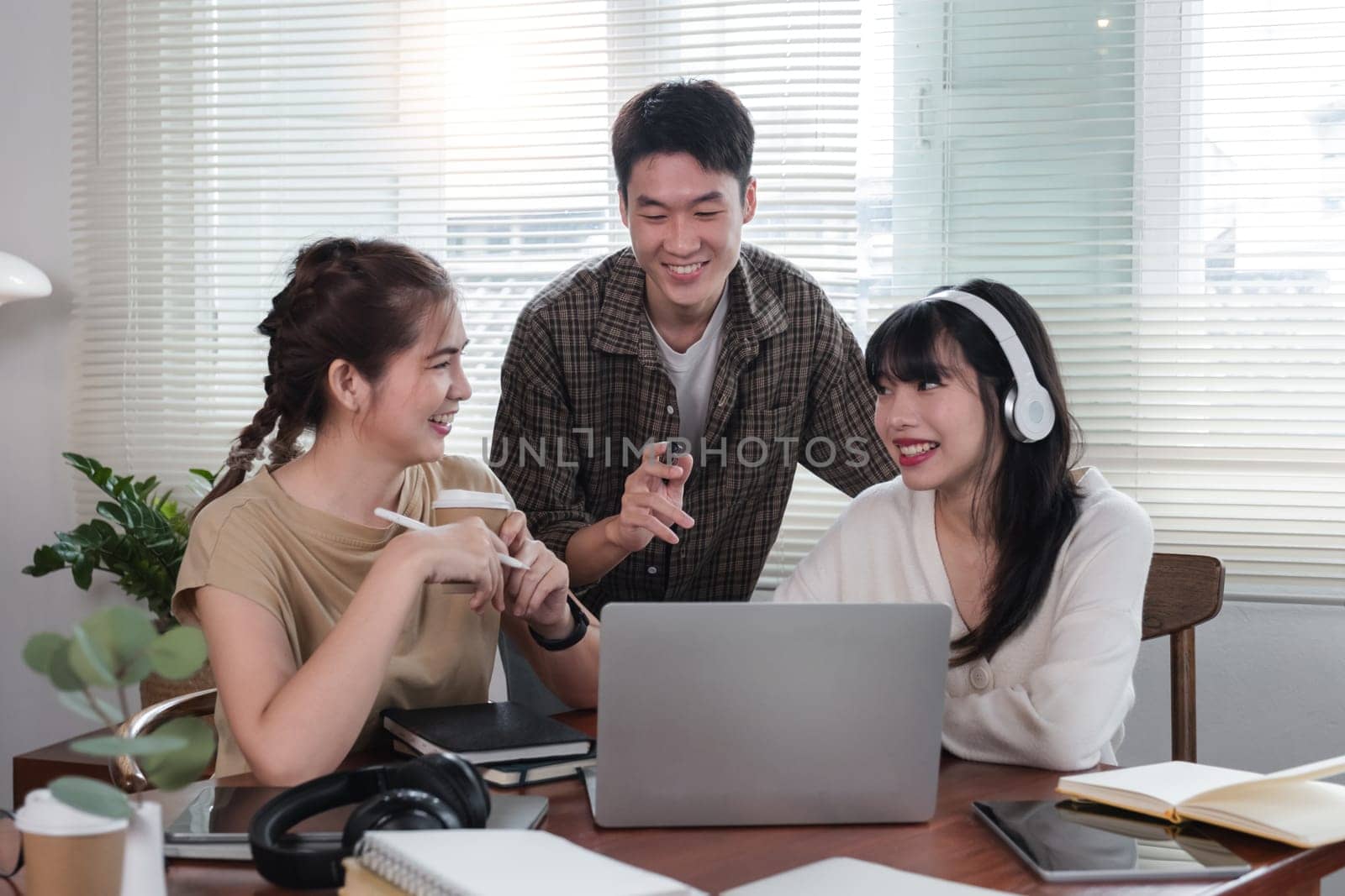 A cheerful and intelligent young Asian man is standing and sharing his thoughts in a meeting with his team. University students, friendship, startups, teamwork by wichayada