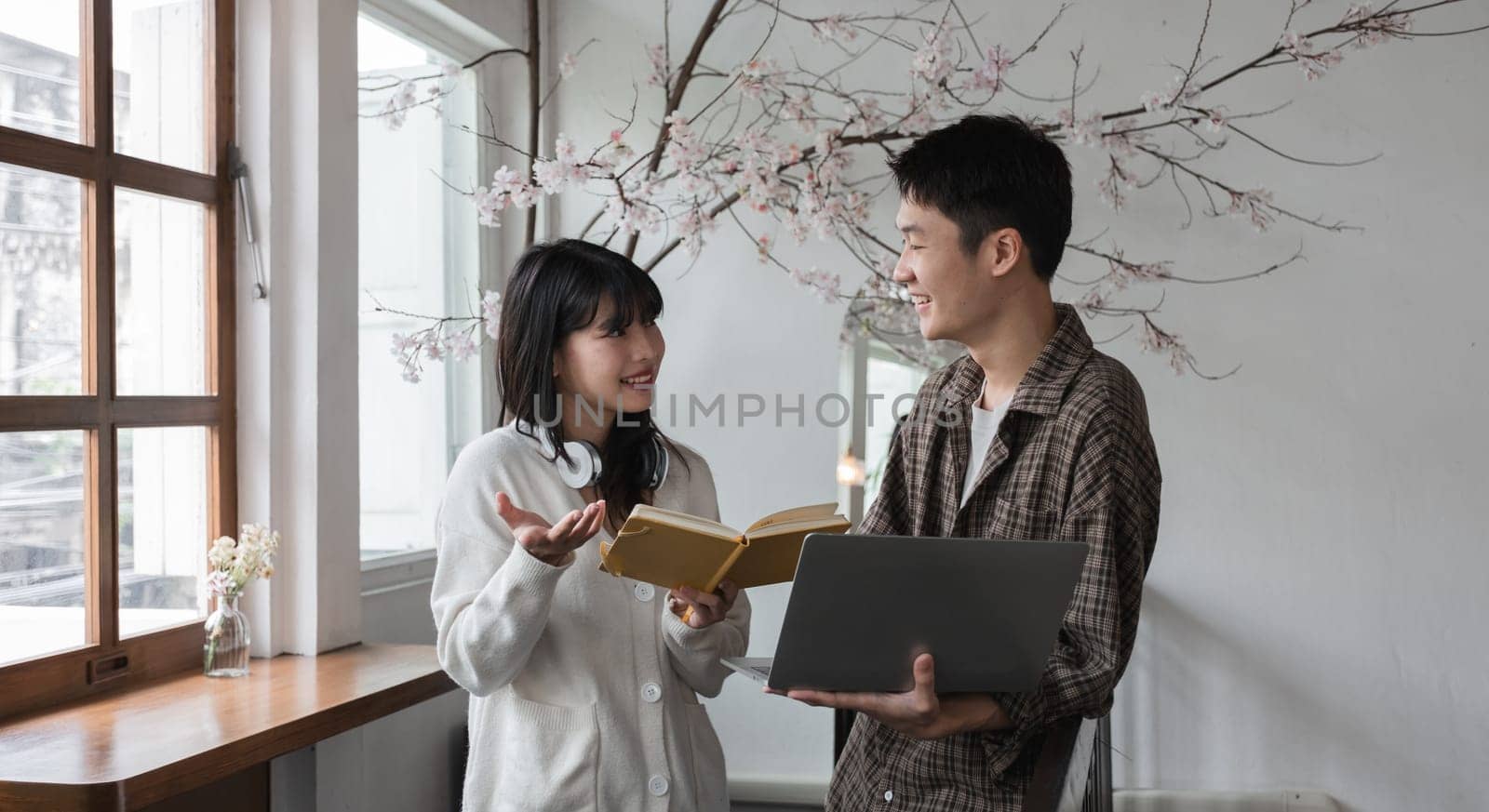 A happy young Asian man and a pretty girl are working on a laptop together, working on a co-project, sharing ideas and discussing work in a room..