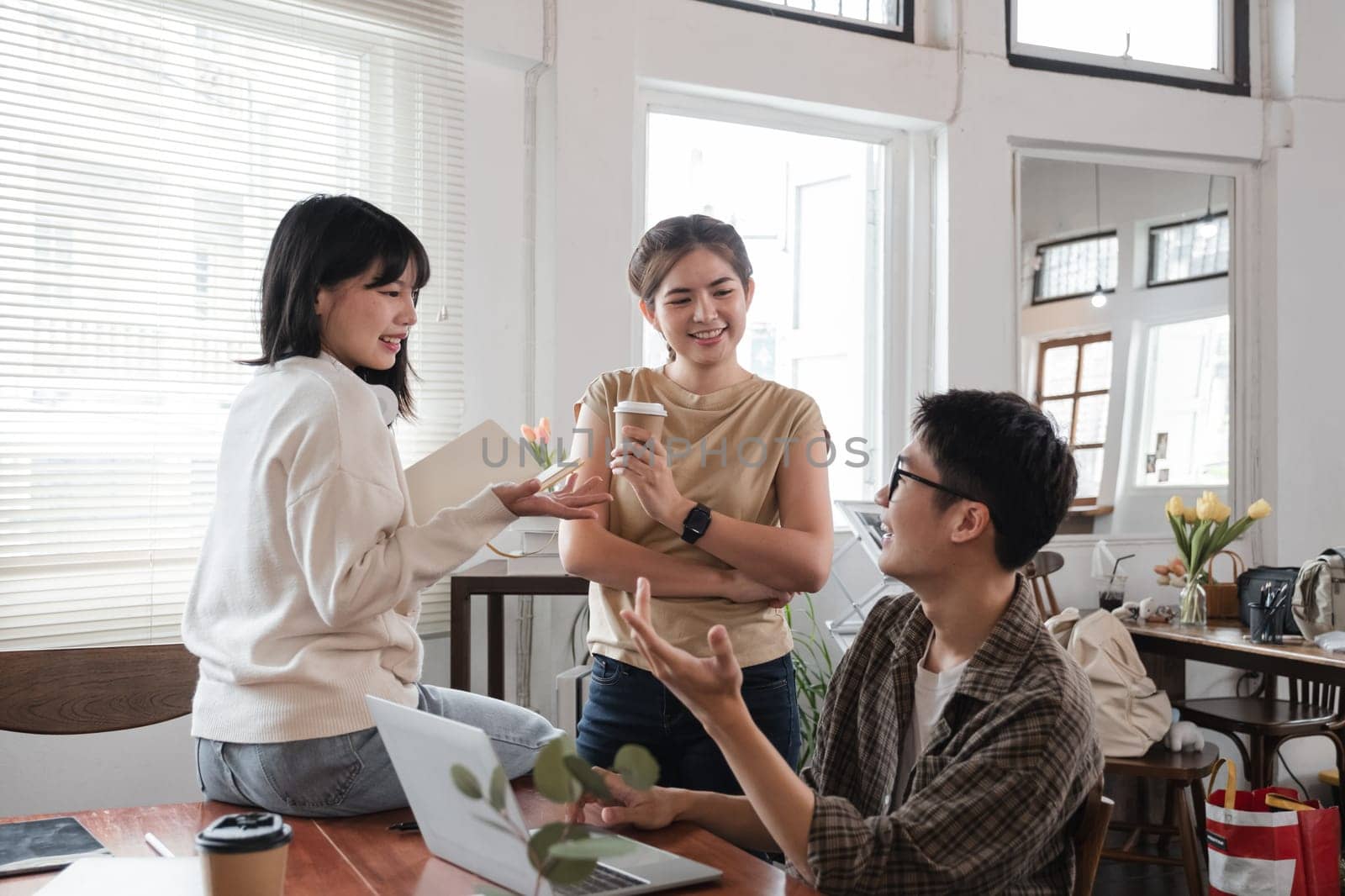 A cheerful and smart young Asian female is standing and sharing her ideas in a meeting with her team. University students, friendship, startups, teamwork.