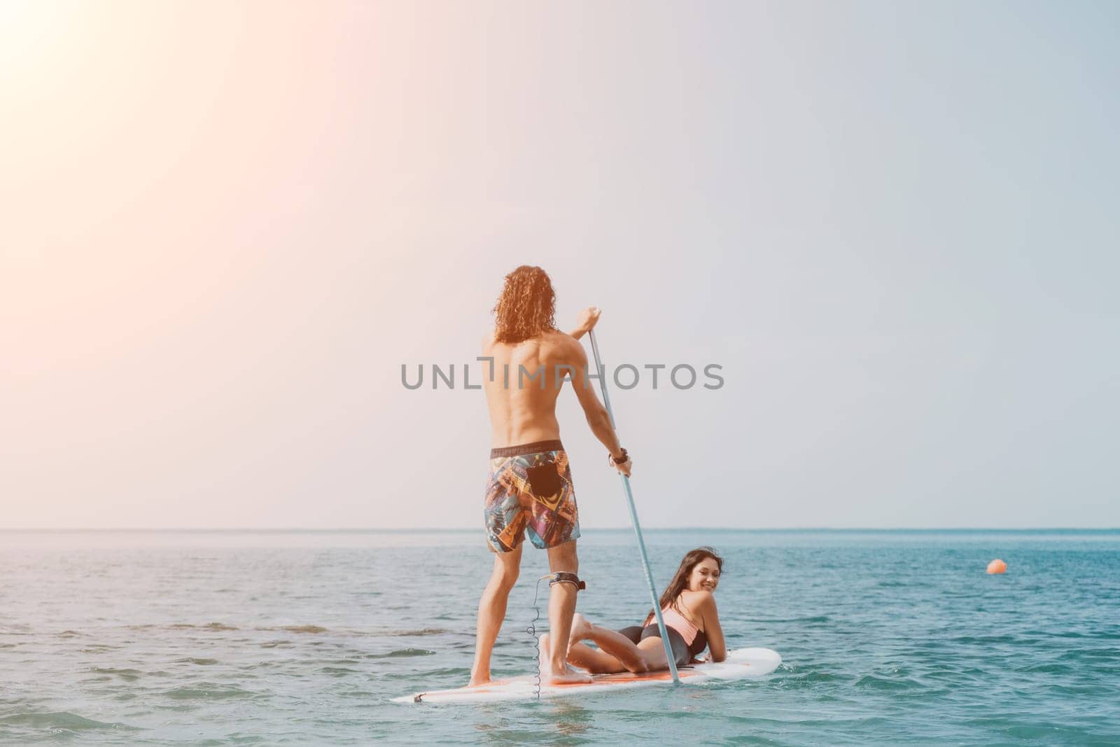 Sea woman and man on sup. Silhouette of happy young woman and man, surfing on SUP board, confident paddling through water surface. Idyllic sunset. Active lifestyle at sea or river