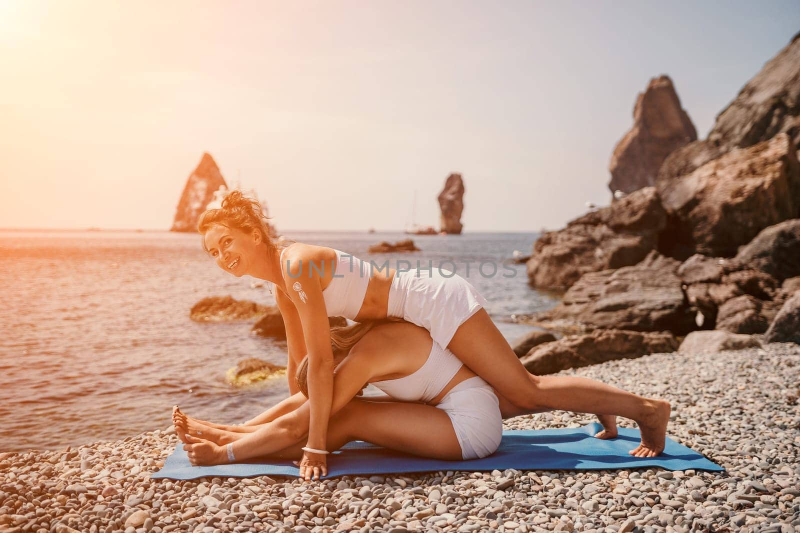 Woman sea yoga. Two happy women practicing yoga on the beach with ocean and rock mountains. Motivation and inspirational fit and exercising. Healthy lifestyle outdoors in nature, fitness concept. by panophotograph