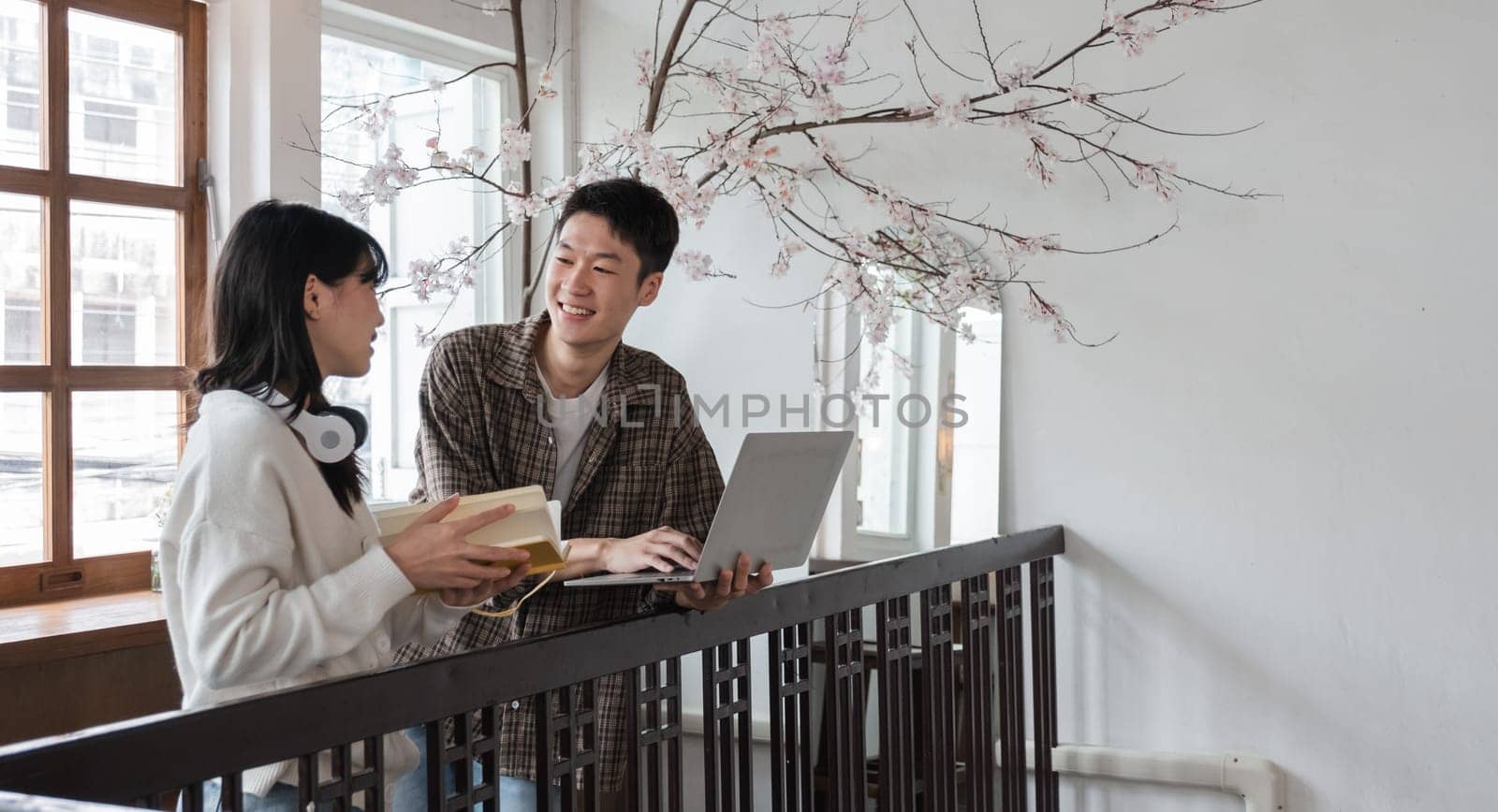 A happy young Asian man and a pretty girl are working on a laptop together, working on a co-project, sharing ideas and discussing work in a room..