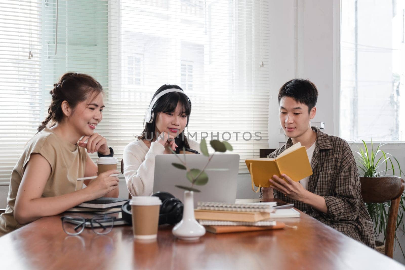 A group of cheerful Asian college students are enjoying talking and discussing their group project while sitting in a coffee shop together..