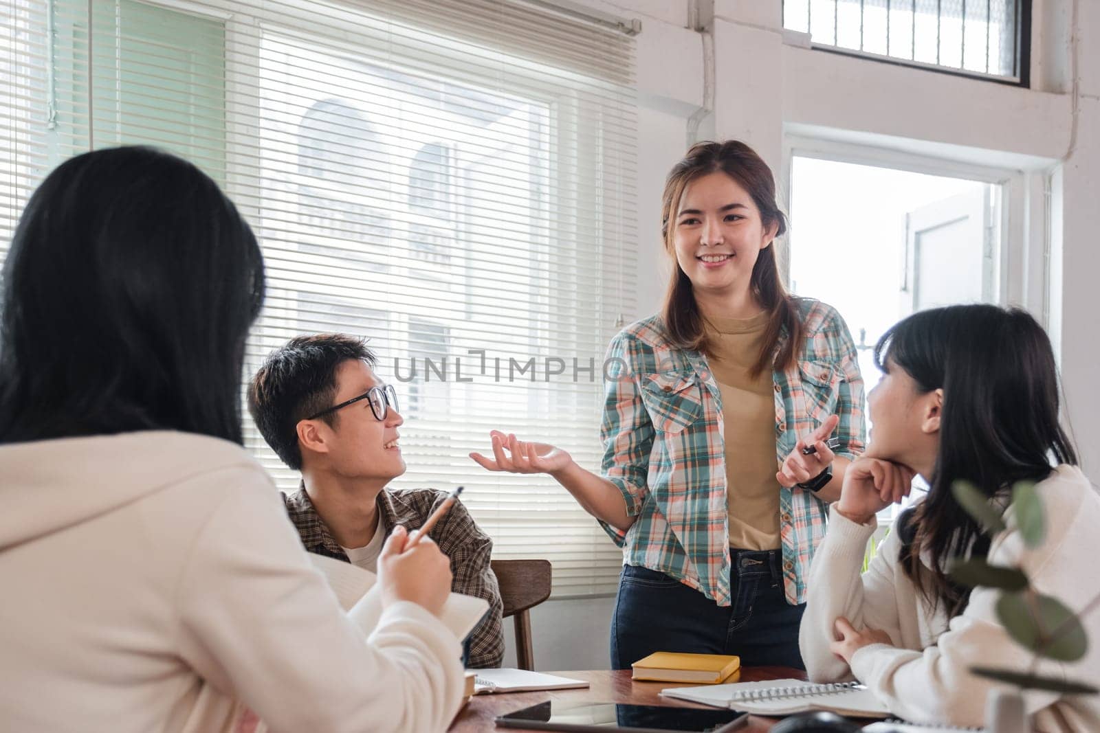 A cheerful and smart young Asian female is standing and sharing her ideas in a meeting with her team. University students, friendship, startups, teamwork.