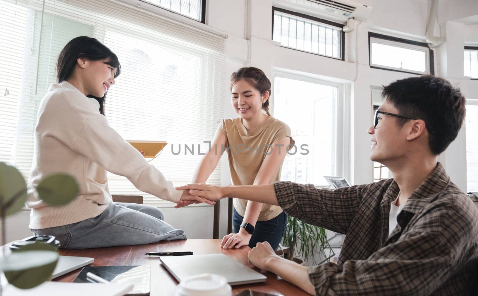 A group of cheerful and happy young Asian friends are gathering together to celebrate the success of a project together in a conference room..