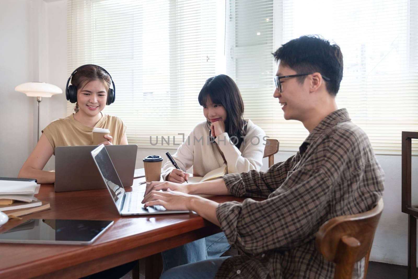 A group of cheerful Asian college students are enjoying talking and discussing their group project while sitting in a coffee shop together..