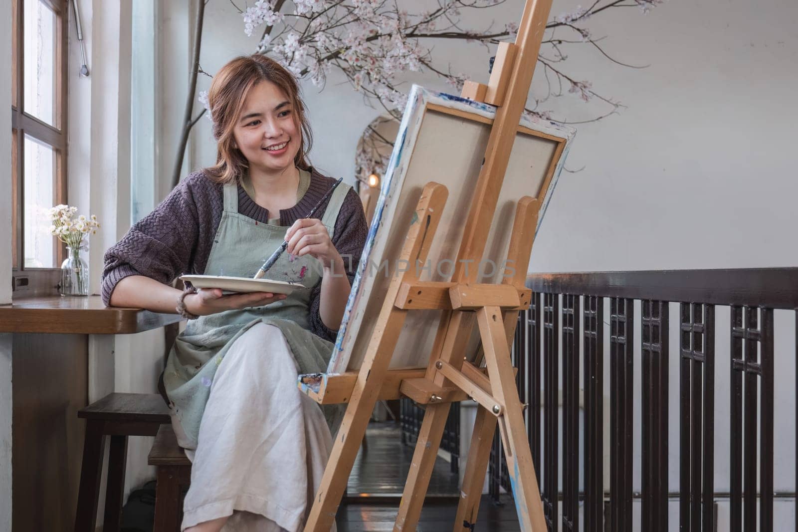 Young female artist works on abstract acrylic painting on canvas in art painting studio. by wichayada