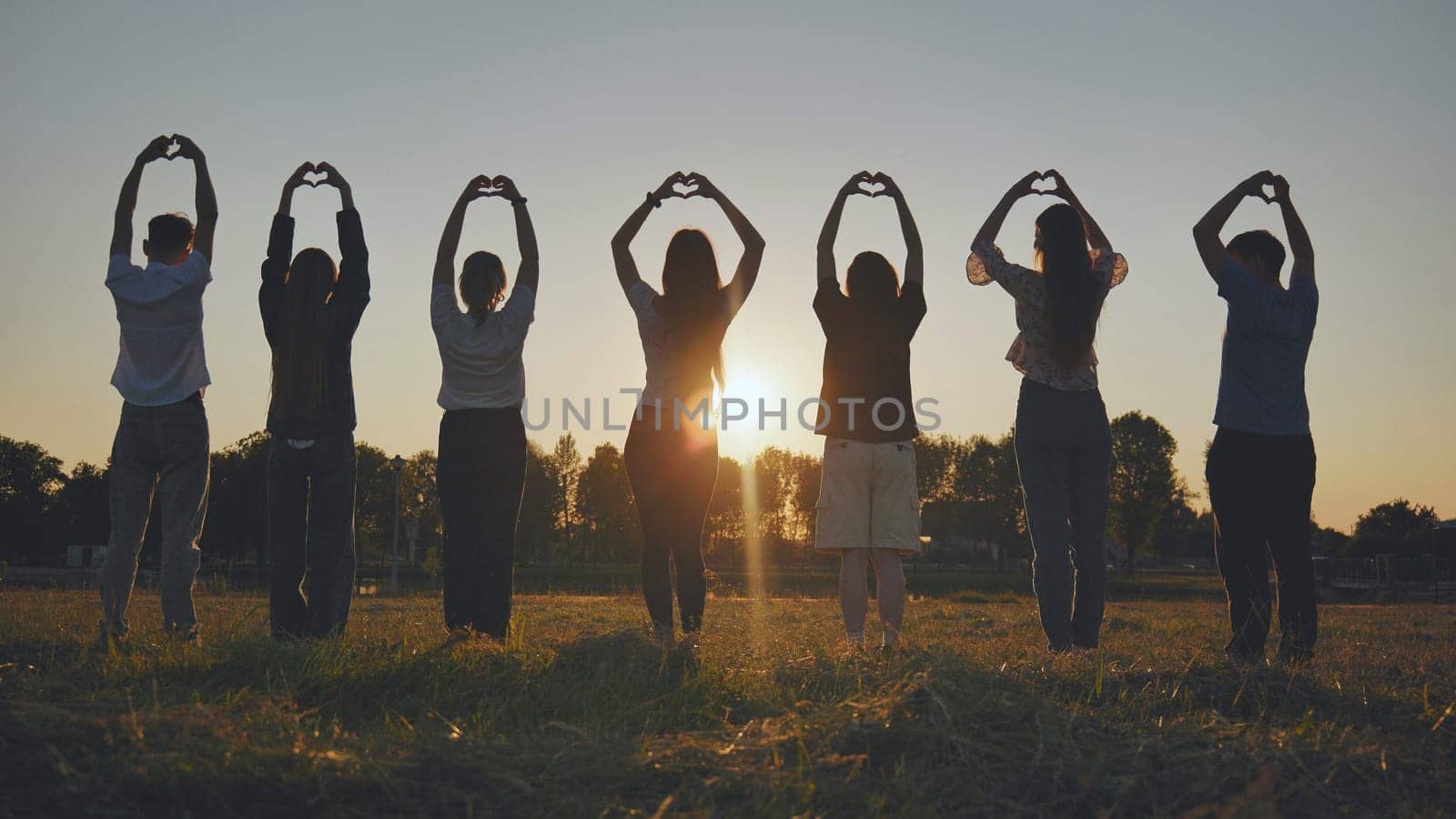 Seven friends make a heart shape from their hands at sunset