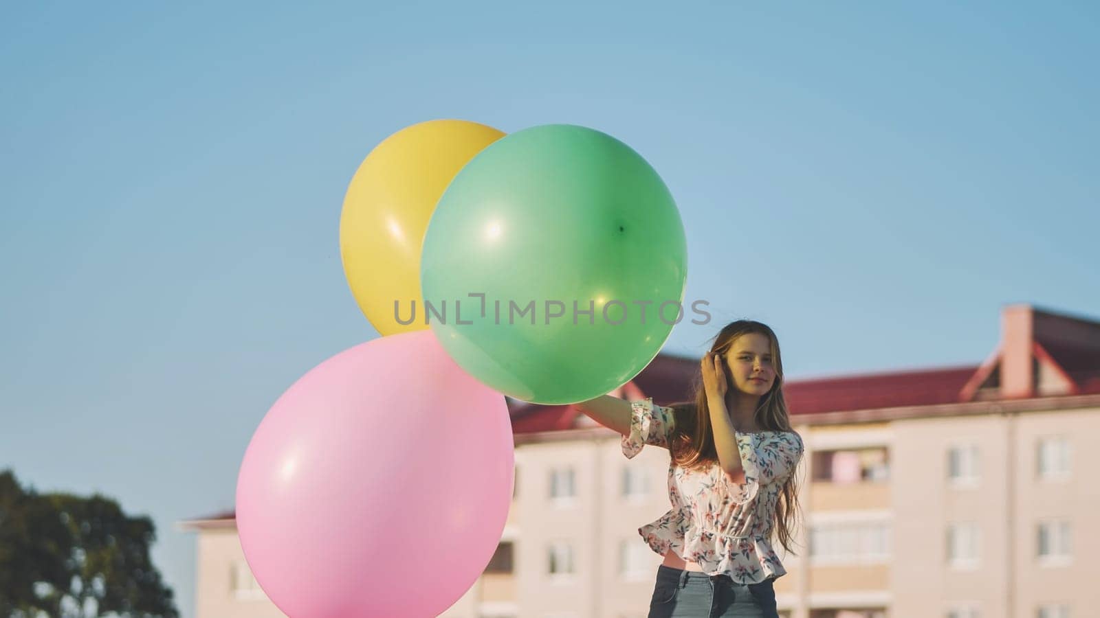 A girl happily poses with large with colorful balloons in the city