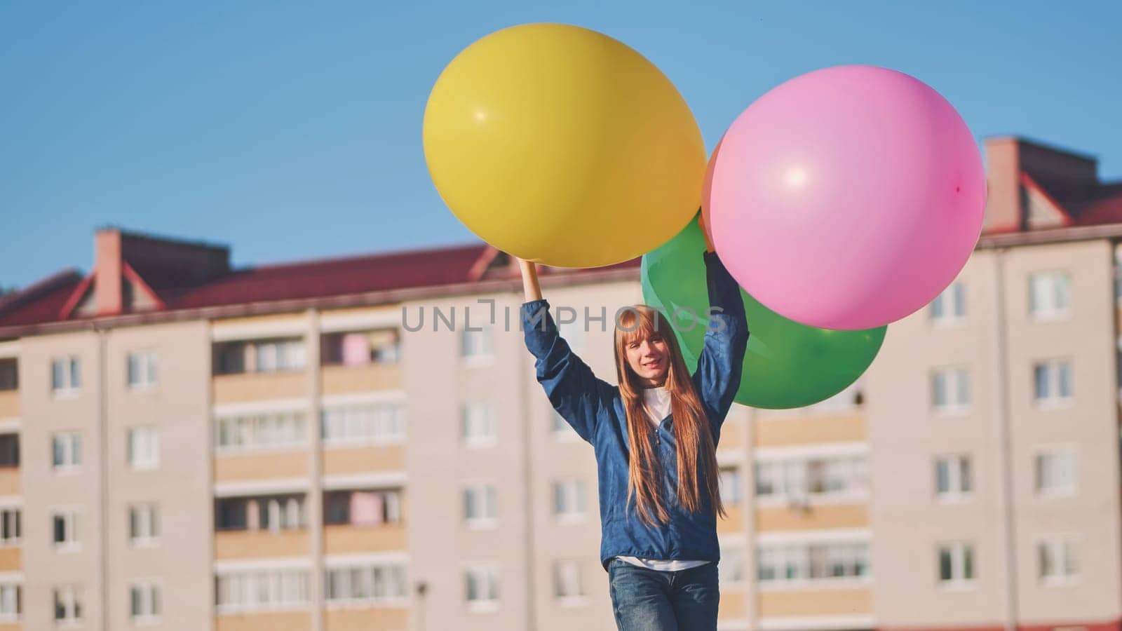 Happy girl with big with colorful balloons posing on the background of city houses