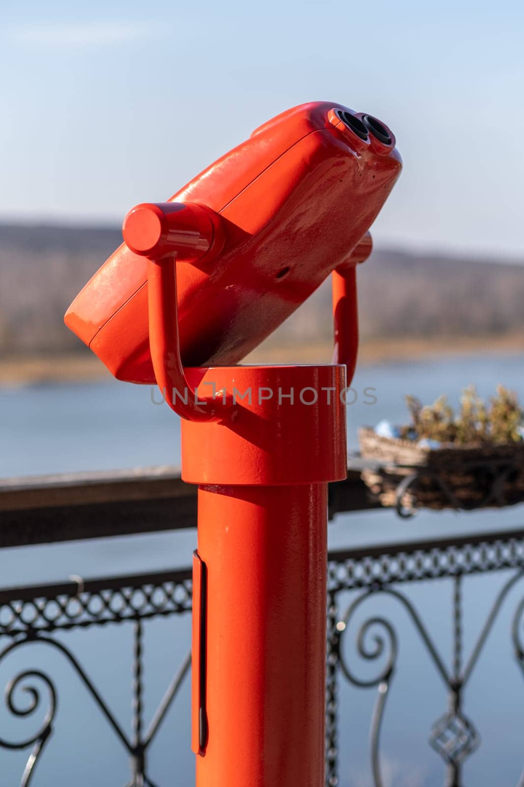 Public stationary binoculars on the banks of the river in summer or autumn to look at nature, coin-operated red metal binoculars.