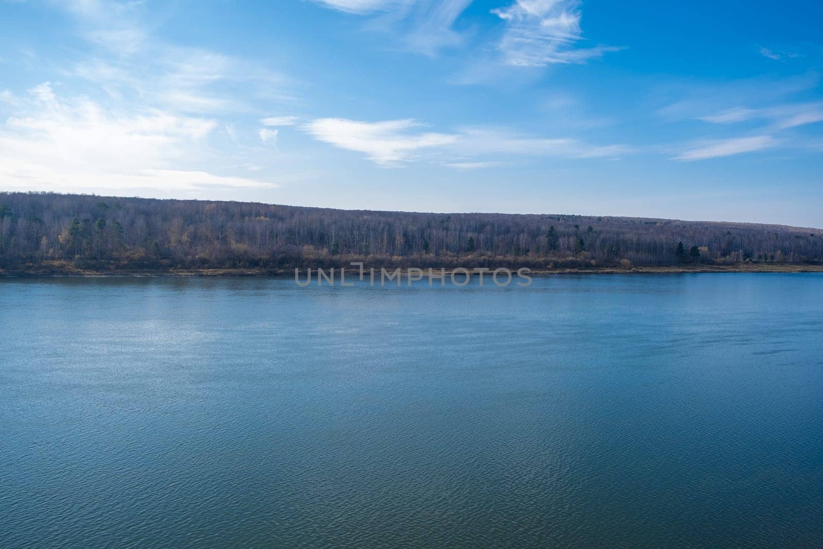 Beautiful, wide autumn river among forests and rocky shore. A calm and quiet place with autumn colors. Reflection of clouds in the water in good weather