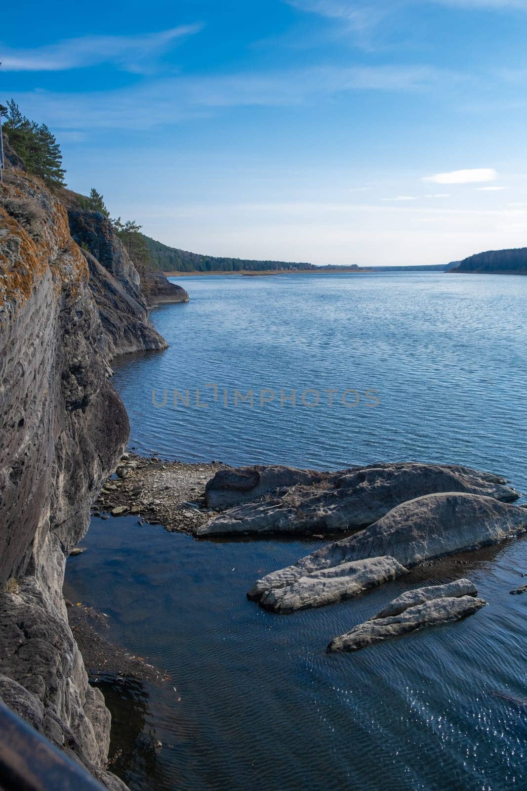 Beautiful, wide autumn river among forests and rocky shore. A calm and quiet place with autumn colors. Reflection of clouds in the water in good weather