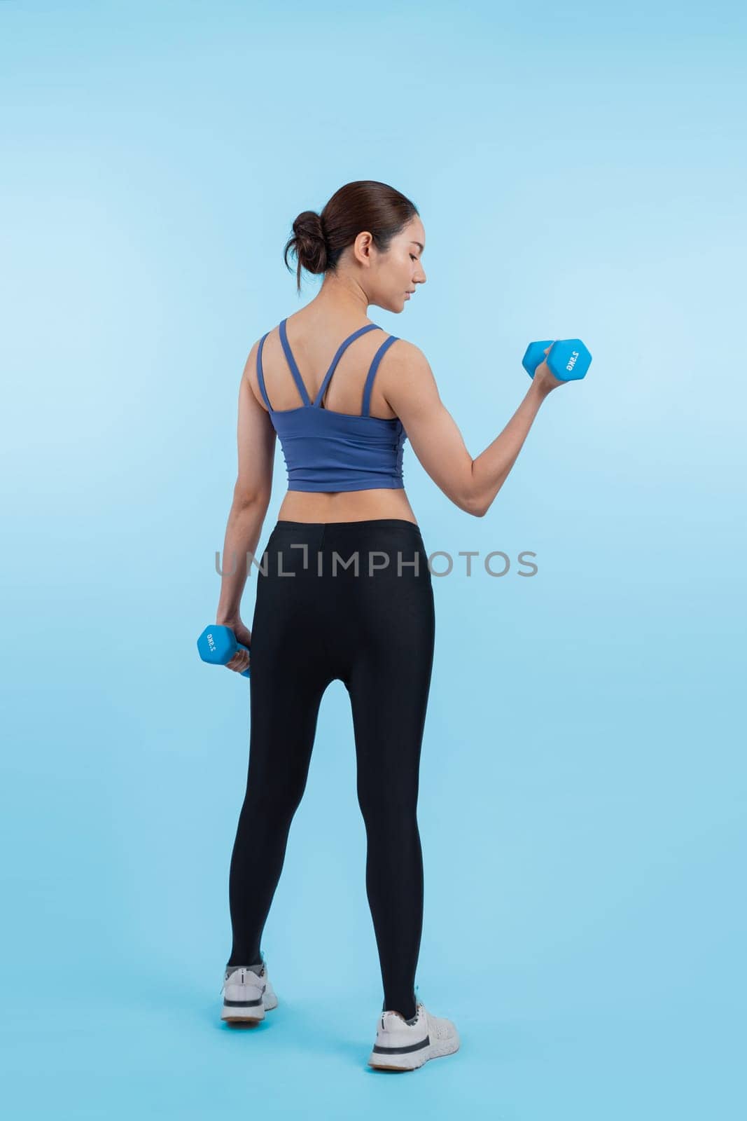 Vigorous energetic woman doing dumbbell weight lifting exercise on isolated background. Young athletic asian woman strength and endurance training session as body workout routine.