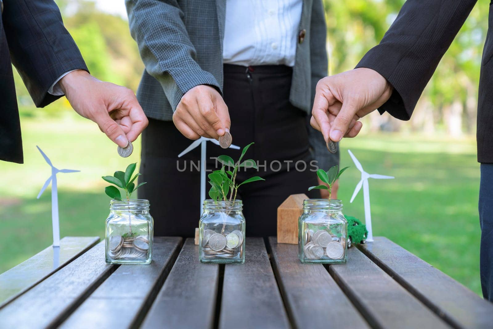 Business people put coin to money saving glass jar on outdoor table as sustainable money growth investment or eco-subsidize. Green corporate promot and invest in environmental awareness. Gyre