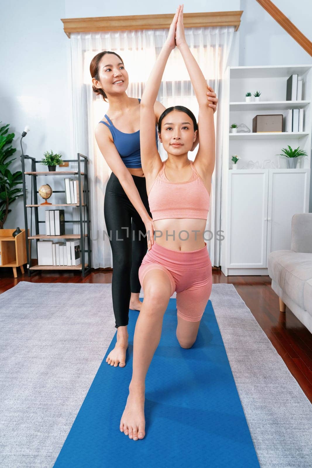 Asian woman doing yoga exercise on fitness mat with trainer. Vigorous by biancoblue