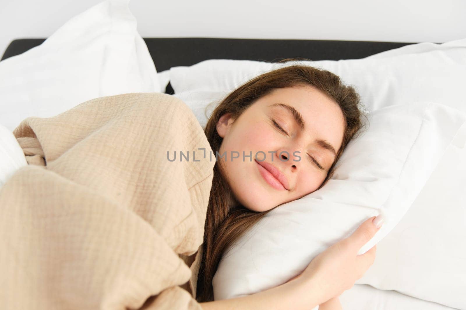 Portrait of smiling brunette woman in pyjamas, sleeping in hotel bed, relaxing with pleased face, dreaming, sleeping in bedroom by Benzoix