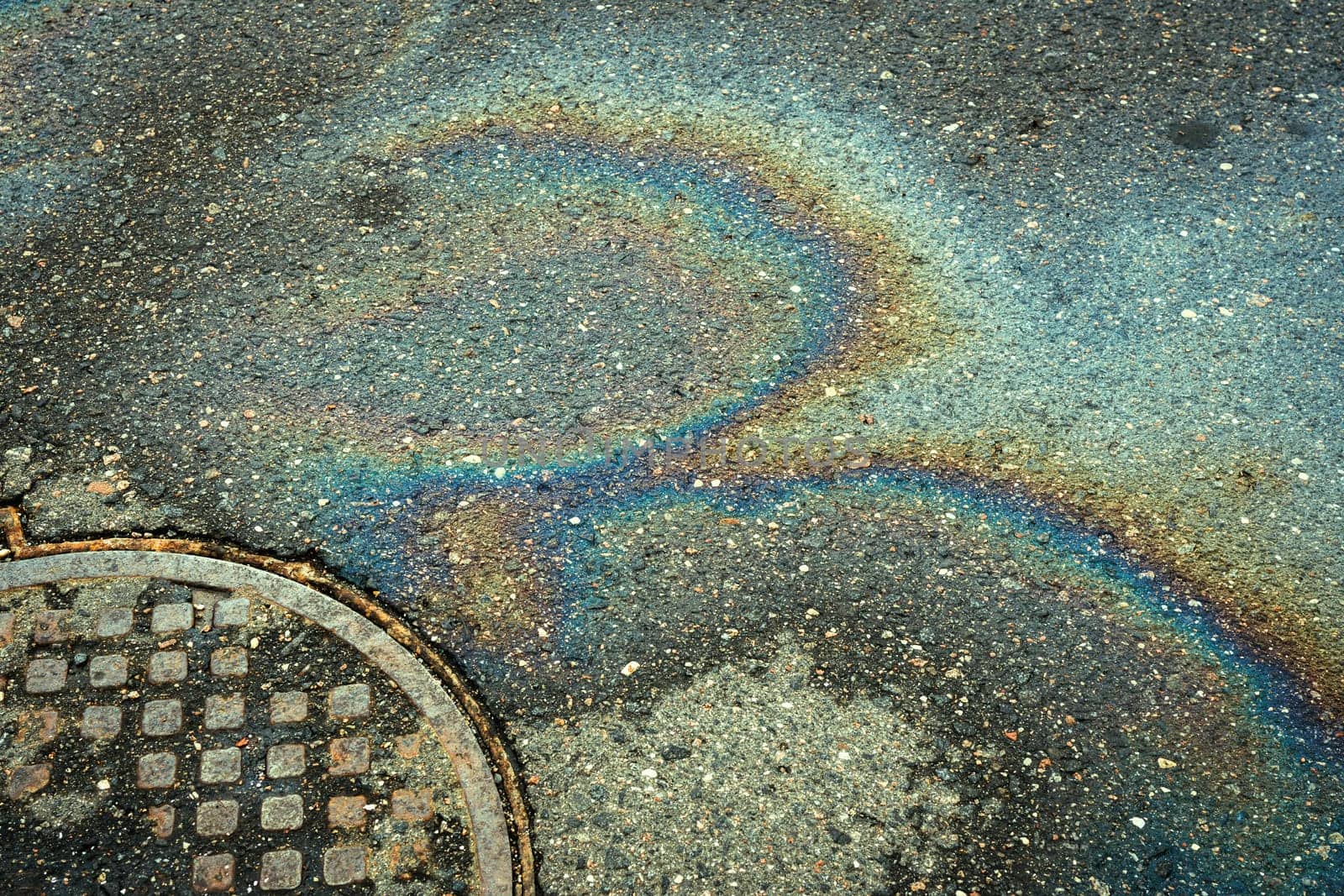 Rainbow stains of gasoline against the background of asphalt and a manhole.