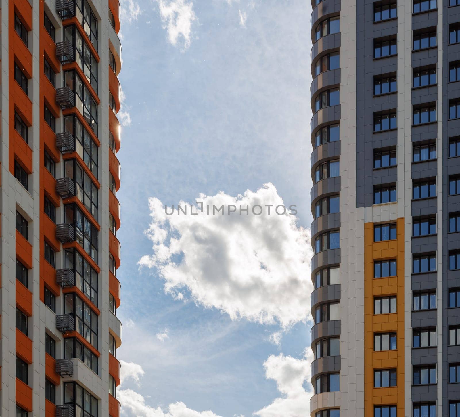freshly built high rise apartment buildings on blue sky background with white clouds.