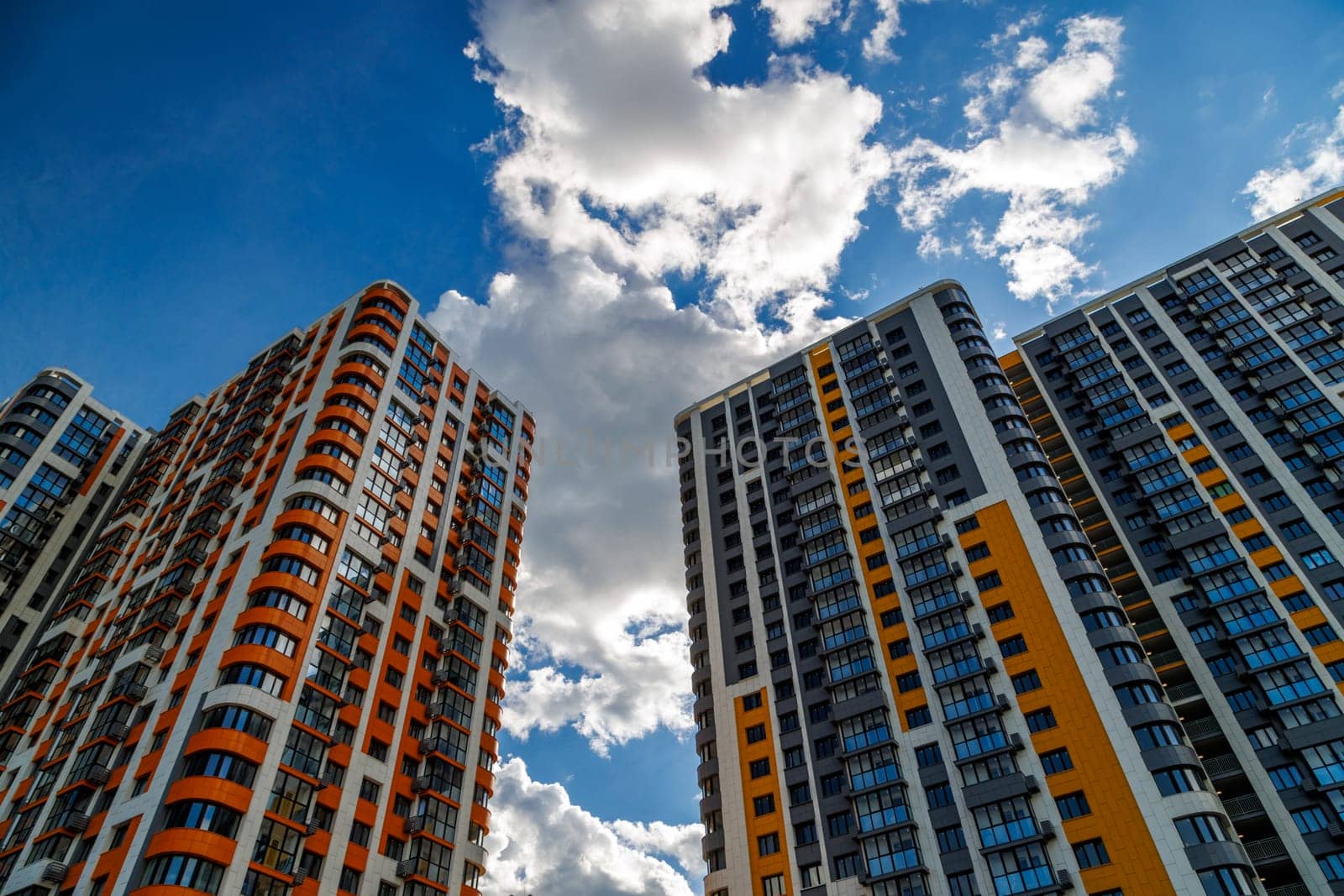 freshly built high rise apartment buildings on blue sky background with white clouds.
