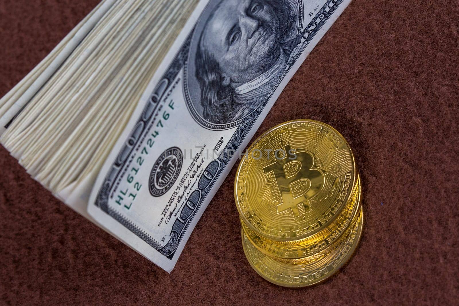 a bunch of us dollar banknotes and three bitcoin shiners on brown fleece background close-up with selective focus