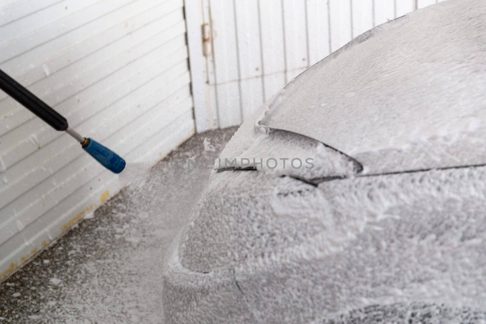process of applying white pressurized non-contact foam to a car from gun for car wash.