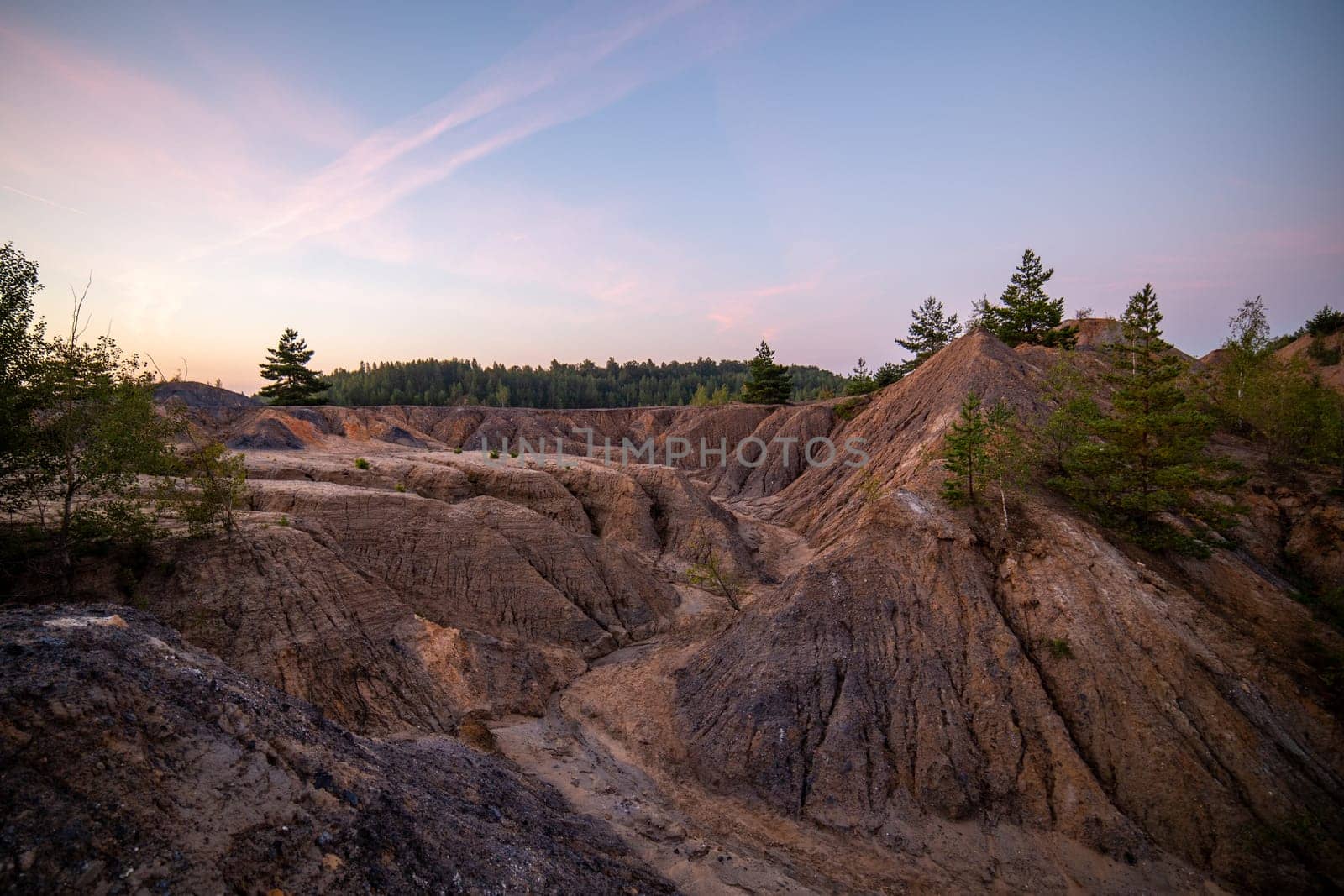 eroded soil quarry ravine with forest on its edge at summer evening.