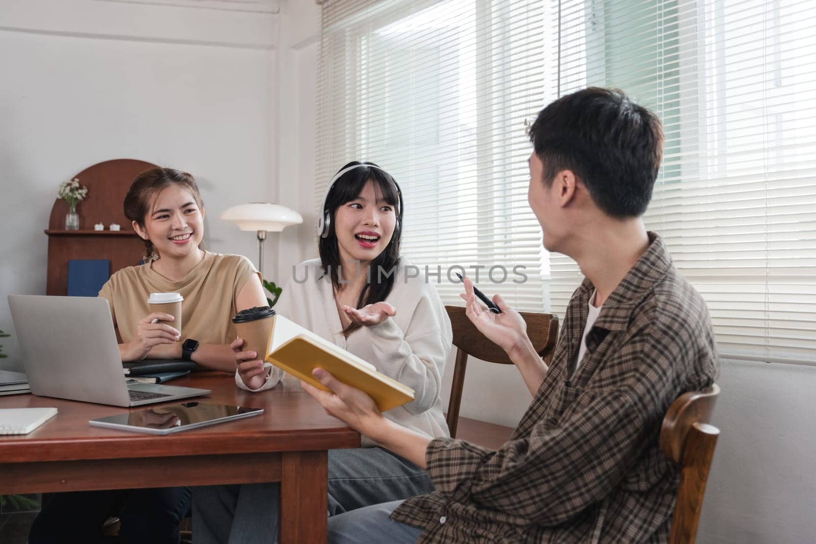 A group of cheerful Asian college students are enjoying talking and discussing their group project while sitting in a coffee shop together. by wichayada