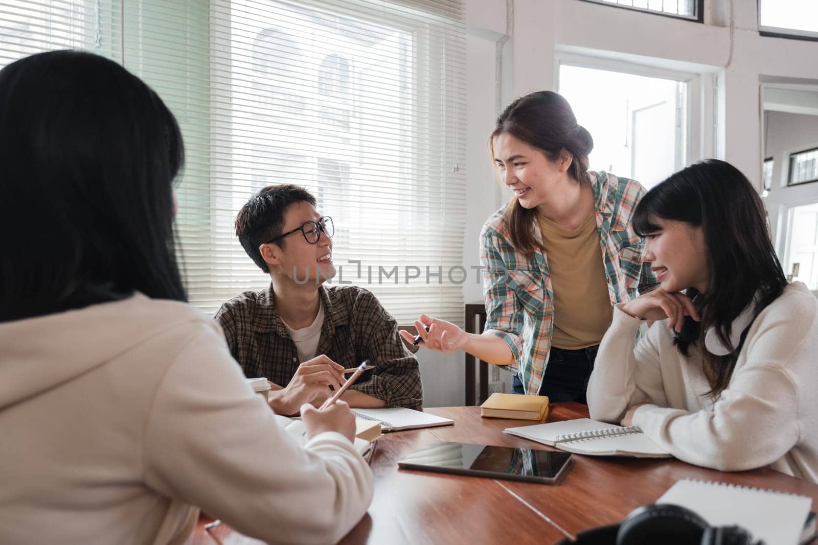 A cheerful and smart young Asian female is standing and sharing her ideas in a meeting with her team. University students, friendship, startups, teamwork by wichayada