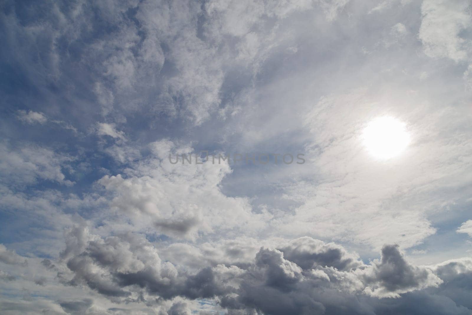blue sky with sun and mixed clouds on different layers, above horizon view.