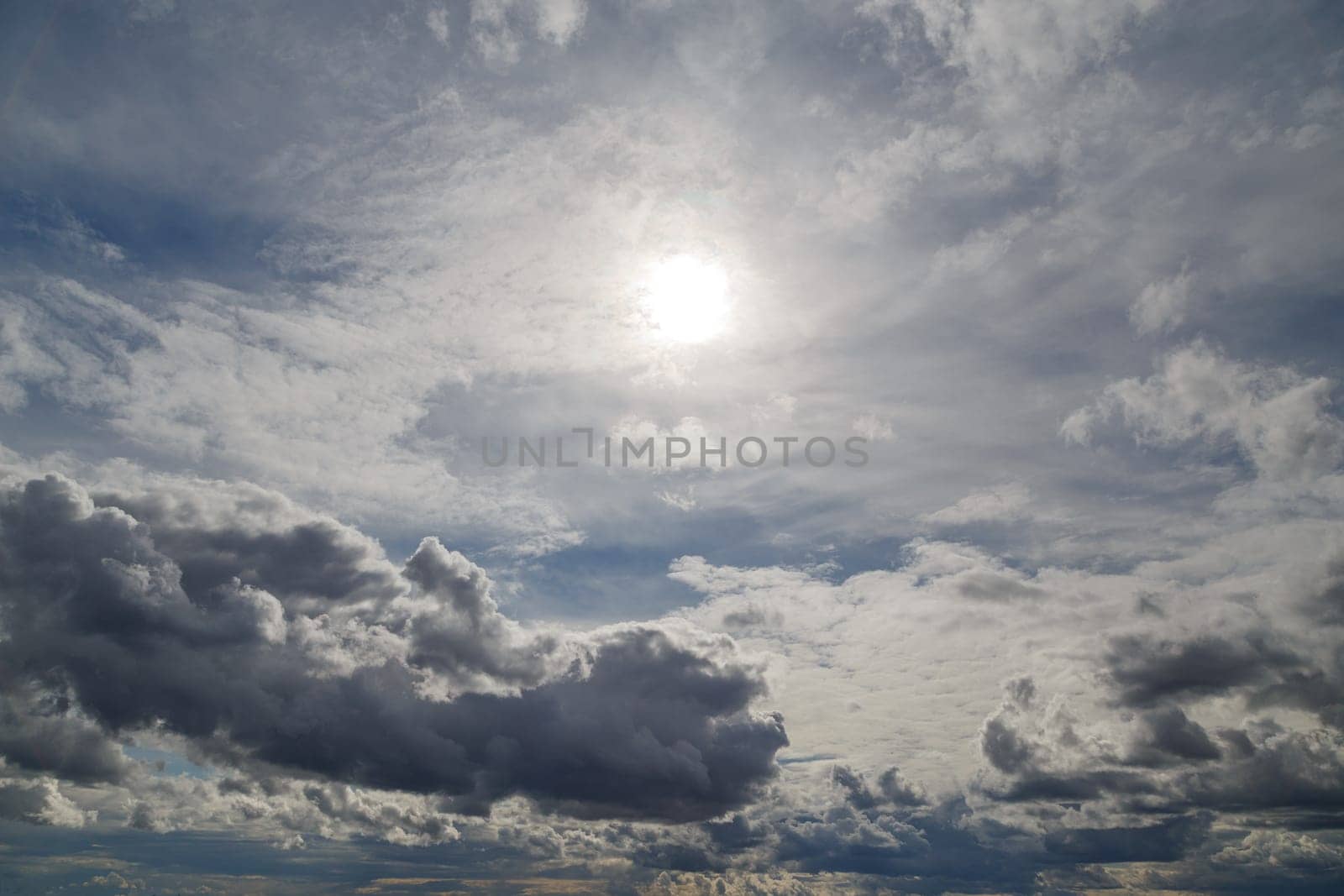 blue sky with sun and mixed clouds on different layers, above horizon view.