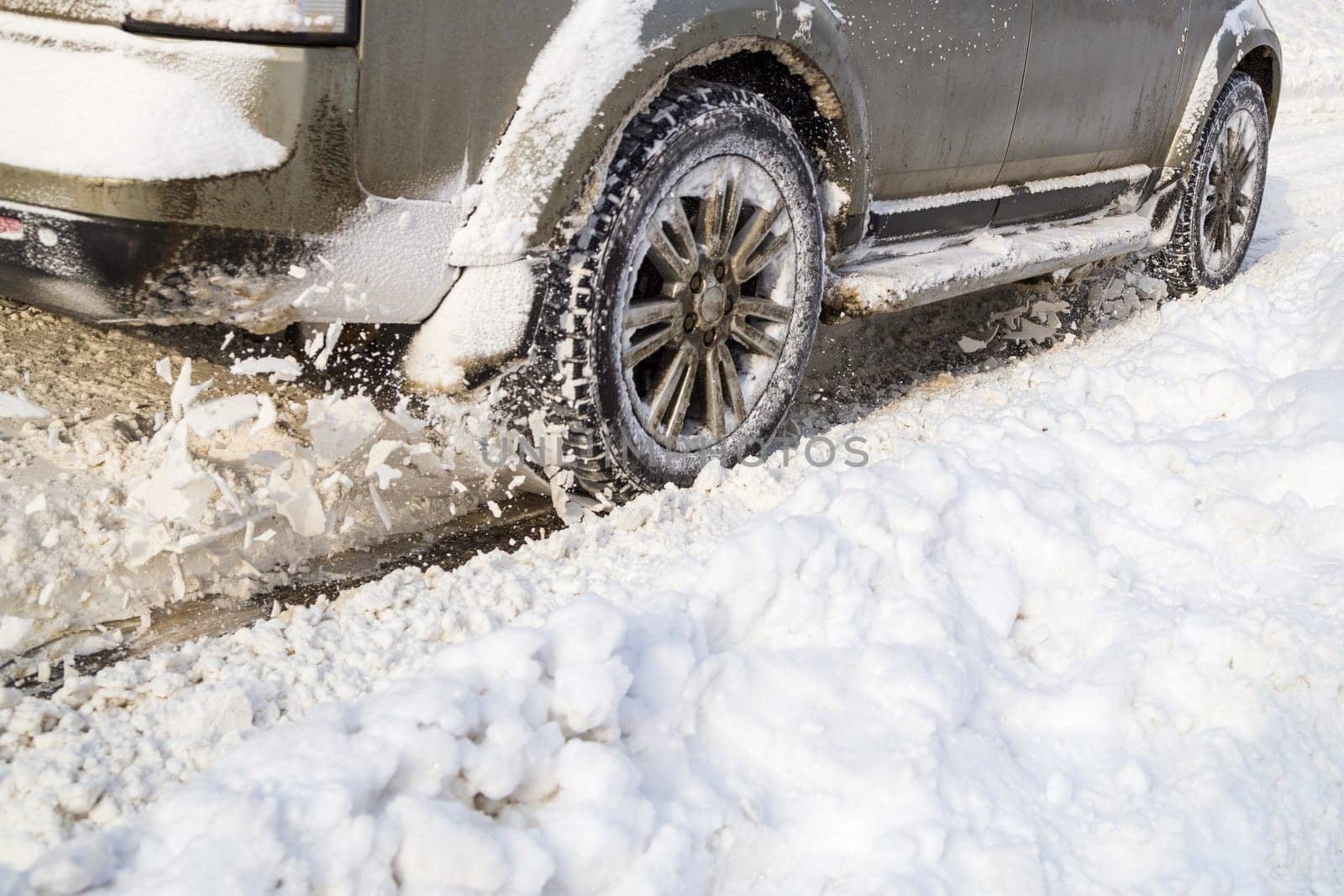 Road snow flies up from a vehicle's spinning wheel. Car's wheels spin and spew up pieces of snow it attempts to gain traction on the slippery road at winter daytime.
