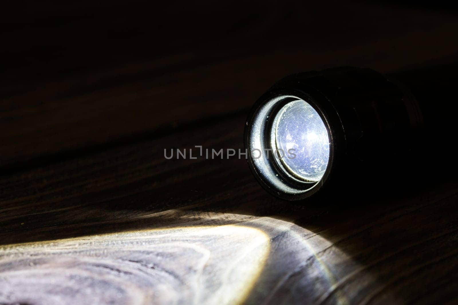 Black led operational flashlight on rough wooden surface - closeup with selective focus.