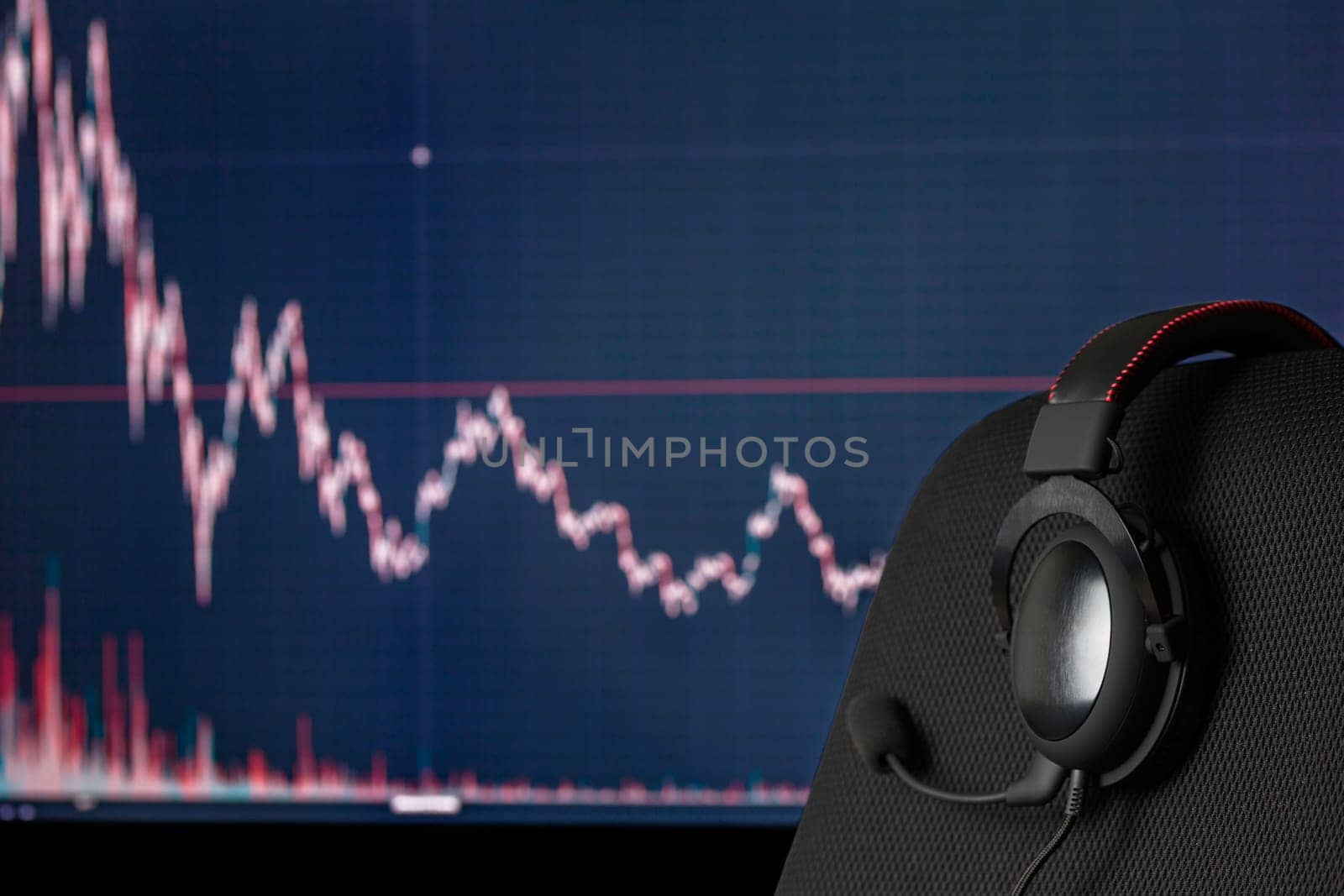 black headset on chair over monitor with trading chart in background - dark background with selective focus and blur